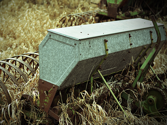 Overgrown by grass and brush, an old seed drill sits unused in South Dakota. (DTN photo by Elaine Kub)